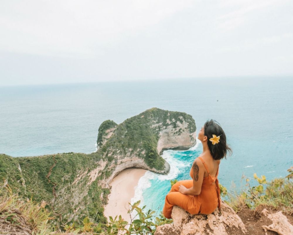 A solo female traveler sitting on the edge of a cliff looking at a beautiful coastal view in Bali, Indonesia