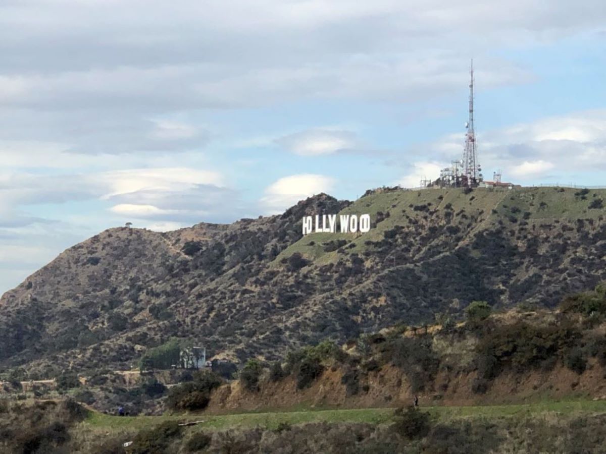 Scenic view of the Hollywood Hills in Los Angeles, California, with the iconic Hollywood sign perched prominently against the hillside. The sprawling urban landscape below contrasts with the natural beauty of the hills, encapsulating the allure of Hollywood's legendary fame and glamour.