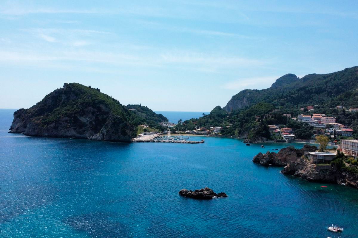 bright blue water meeting the coast of Paleokastritsa and its hillside dotted with houses in Corfu, Greece