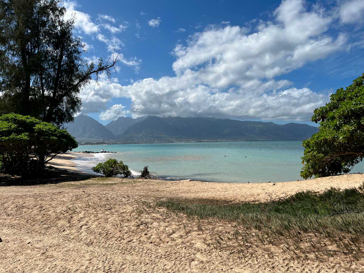 golden sand of Kanaha Beach looking out toward rolling mountains and coastline of Maui, Hawaii
