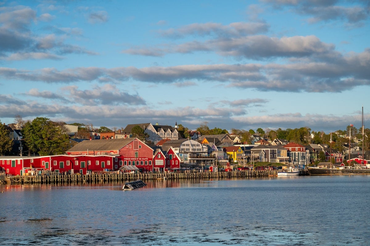 Scenic view of Lunenburg’s colorful waterfront from Lightship Brewery, featuring red historic buildings like the Fisheries Museum of the Atlantic and charming houses along the shore under a partly cloudy sky.