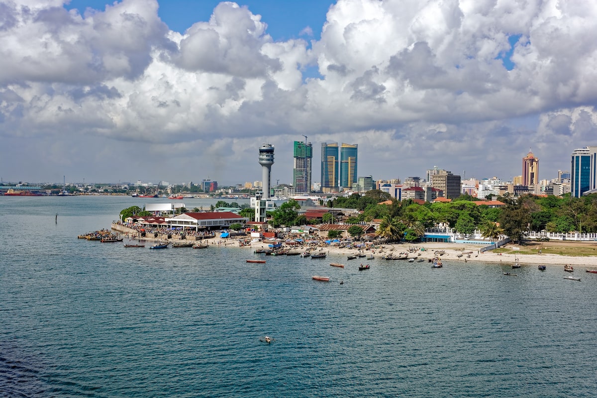 Skyline view of Dar es Salaam, Tanzania, featuring modern buildings, a bustling waterfront, and small boats along the shore.