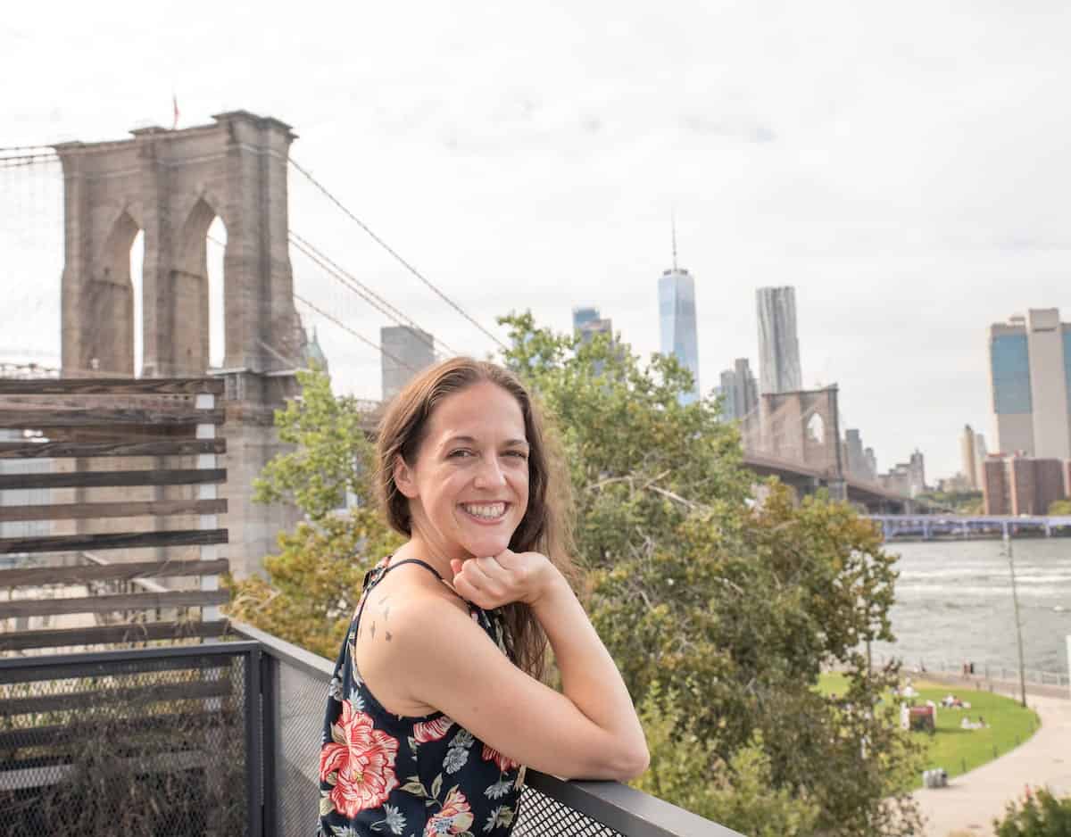 woman smiling at the camera with the Manhattan skyline in the background in DUMBO, Brooklyn