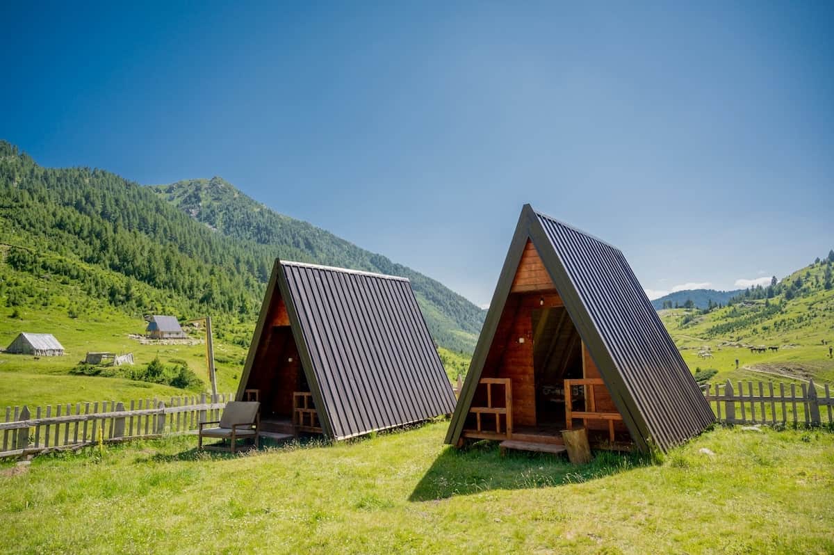 A-frame wooden cabins at Leonardi Guesthouse in Doberdol, surrounded by lush green meadows and mountains on the Peaks of the Balkans trail.