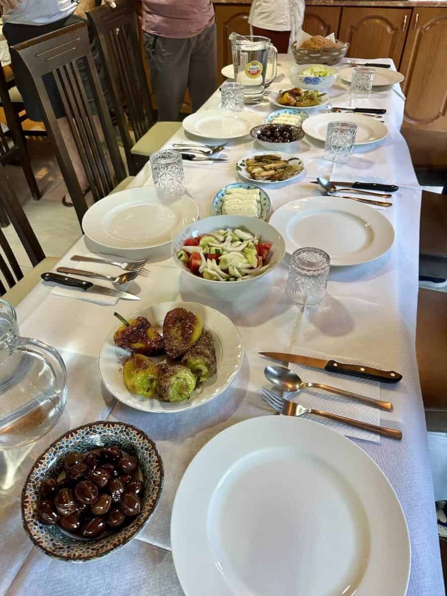 A table set for a meal with plates of vegetarian appetizers including olives, grilled peppers, fresh salad, cheese, and bread, at a guesthouse along the Peaks of the Balkans trail.