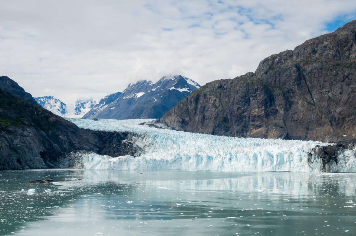Close-up view of the striking blue ice of Margerie Glacier in Glacier Bay National Park, Alaska, framed by rugged mountain peaks and calm reflective waters.